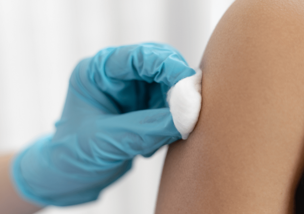 image, blue gloved hand applying disinfectant on upper arm prior to vaccination