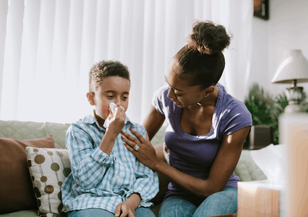 Concerned mother comforts her son blowing his nose indoors, managing spring breathing issues in Texas caused by allergies.