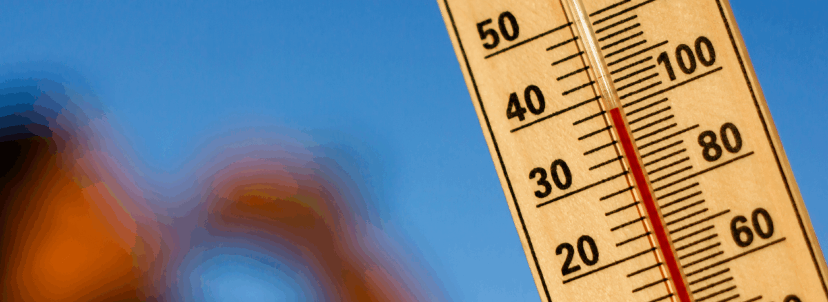 Close-up of a thermometer showing temperatures over 100°F with a blurred figure drinking water in the background, emphasizing dangerous late-summer heat