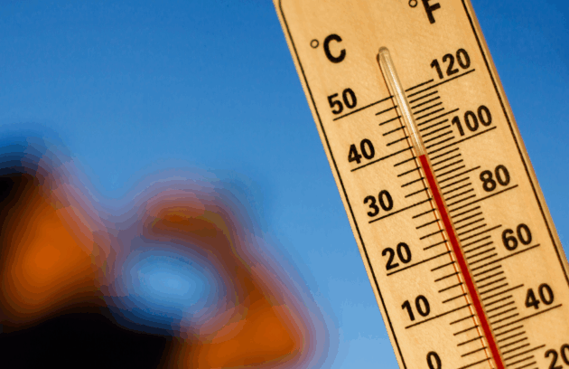 Close-up of a thermometer showing temperatures over 100°F with a blurred figure drinking water in the background, emphasizing dangerous late-summer heat
