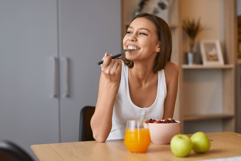 Woman enjoying a healthy breakfast with fruit and juice, supporting digestion and gut function.