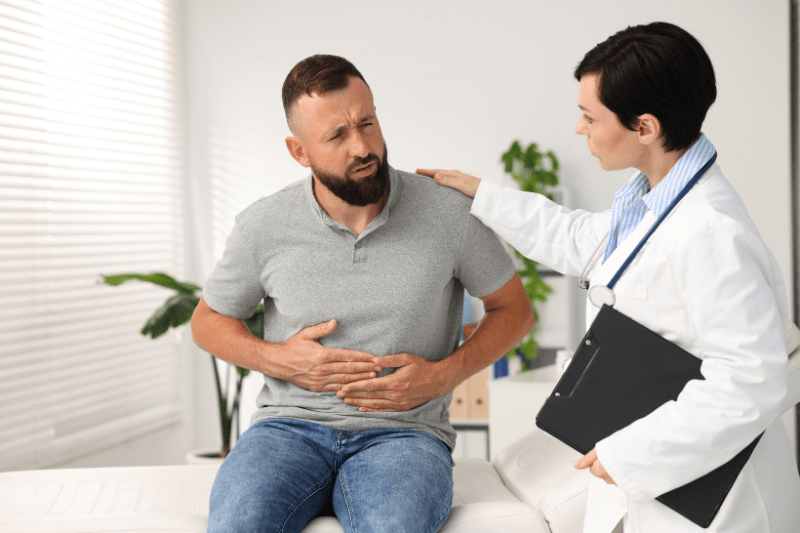 Man experiencing abdominal pain while consulting with a healthcare provider in a medical office.
